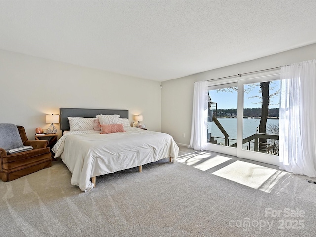 carpeted bedroom featuring access to outside, visible vents, a water view, and a textured ceiling