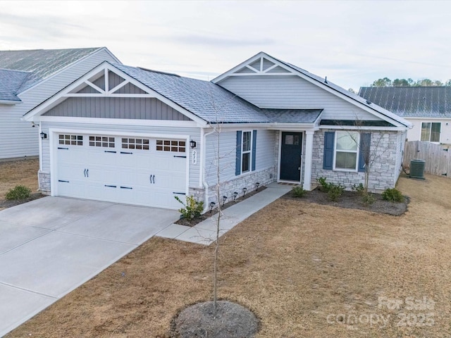 view of front of home featuring central air condition unit, a shingled roof, an attached garage, stone siding, and driveway