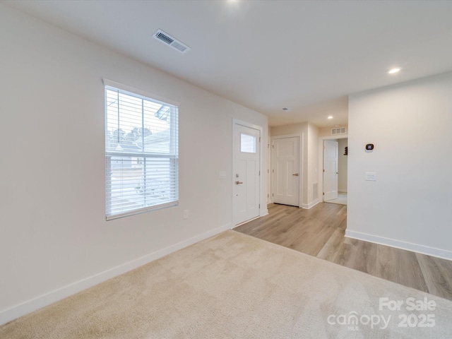 foyer entrance featuring light carpet, baseboards, and visible vents