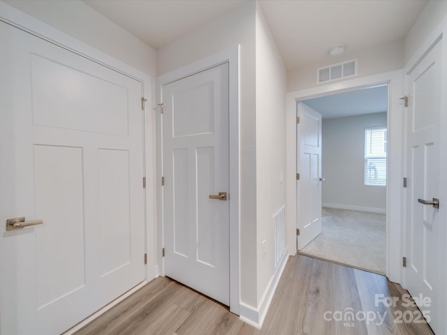 hallway featuring light wood-type flooring, visible vents, and baseboards