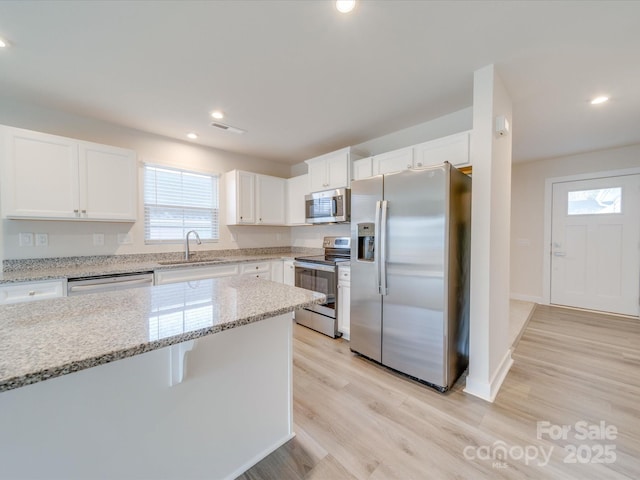 kitchen featuring white cabinets, light stone counters, stainless steel appliances, light wood-type flooring, and a sink