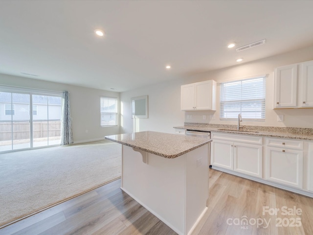 kitchen featuring visible vents, light stone counters, a sink, and a center island