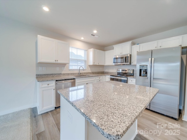 kitchen with a sink, white cabinetry, appliances with stainless steel finishes, light wood-type flooring, and a center island