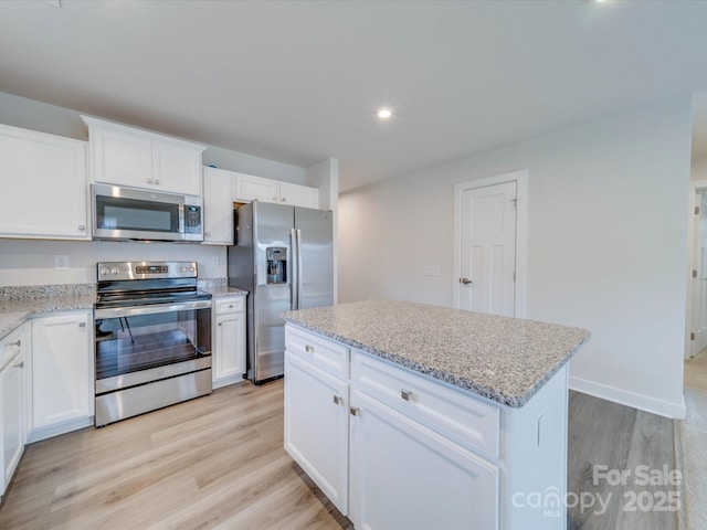 kitchen featuring light stone countertops, light wood-style flooring, appliances with stainless steel finishes, and white cabinets