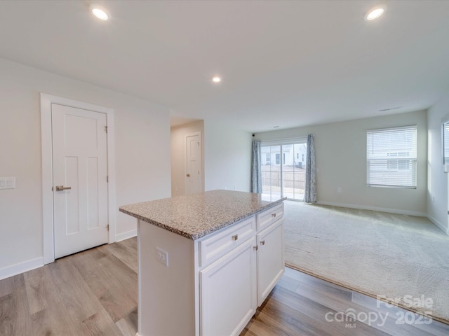 kitchen with recessed lighting, a center island, white cabinetry, open floor plan, and light stone countertops