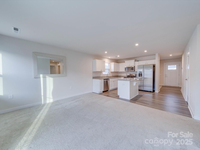 kitchen with light colored carpet, a kitchen island, white cabinets, open floor plan, and appliances with stainless steel finishes