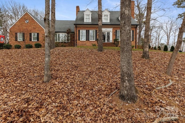 view of front facade with french doors, brick siding, and a chimney