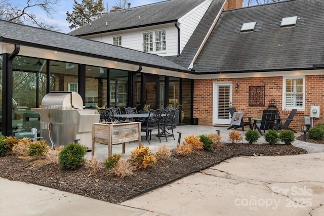 rear view of house featuring a patio, brick siding, exterior kitchen, roof with shingles, and a chimney