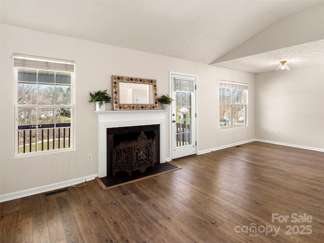 unfurnished living room with a fireplace with raised hearth, lofted ceiling, hardwood / wood-style flooring, visible vents, and baseboards