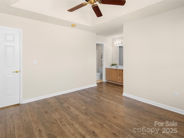 empty room with a ceiling fan, a tray ceiling, dark wood-style flooring, and baseboards