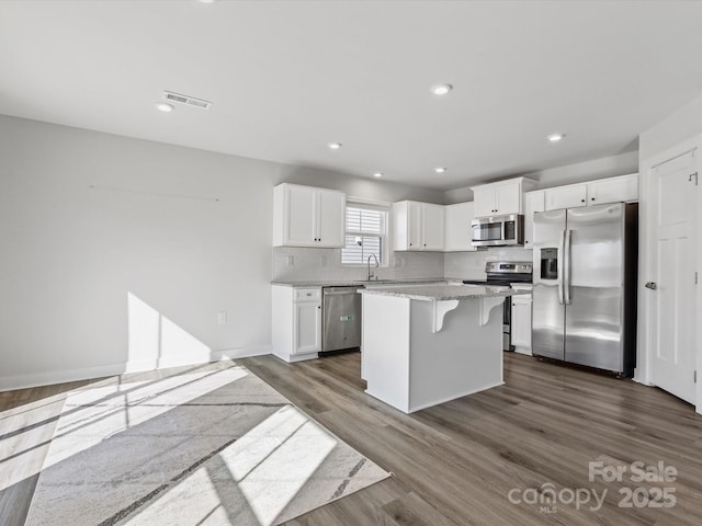 kitchen featuring appliances with stainless steel finishes, dark wood-type flooring, a sink, white cabinetry, and backsplash