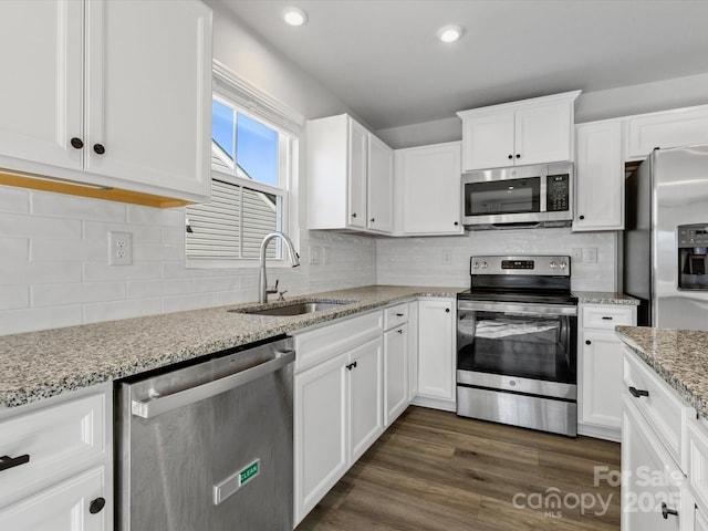 kitchen with dark wood finished floors, stainless steel appliances, decorative backsplash, white cabinets, and a sink