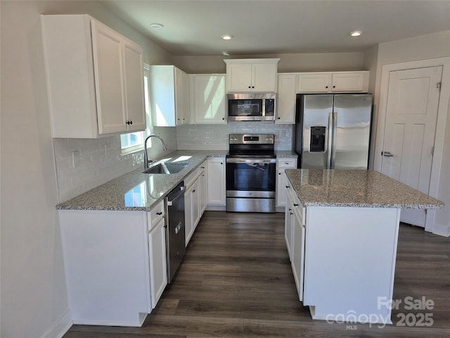 kitchen with a kitchen island, appliances with stainless steel finishes, light stone counters, dark wood-style flooring, and a sink