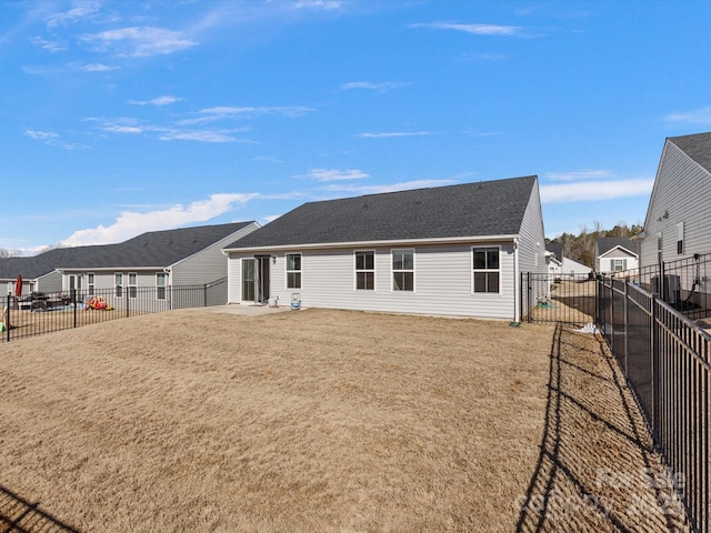 back of house with roof with shingles, a fenced backyard, a yard, and a patio