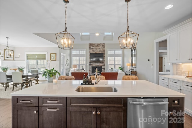 kitchen with a sink, dark brown cabinetry, stainless steel dishwasher, and an inviting chandelier