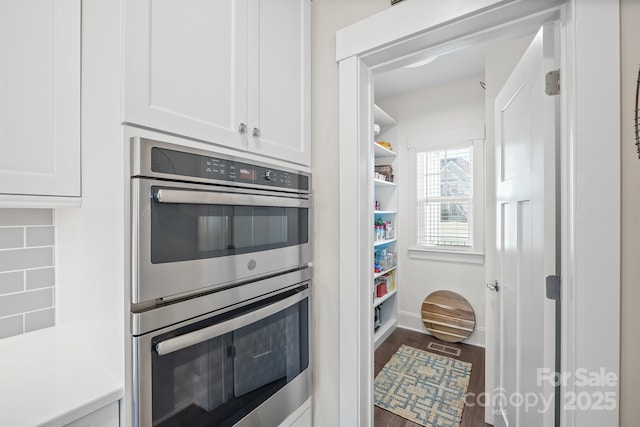 kitchen with baseboards, white cabinets, stainless steel double oven, and wood finished floors