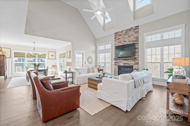 living area featuring visible vents, wood finished floors, a fireplace, high vaulted ceiling, and ceiling fan with notable chandelier