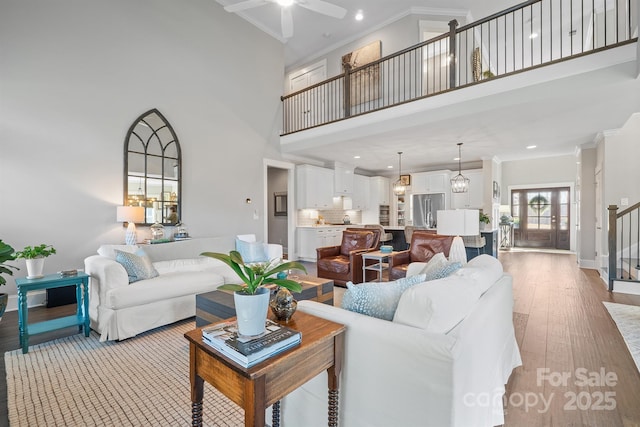 living area with a towering ceiling, ceiling fan, ornamental molding, stairs, and light wood-type flooring