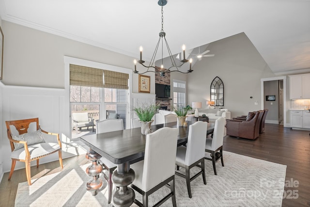 dining area featuring a chandelier, lofted ceiling, a wainscoted wall, dark wood-style floors, and crown molding