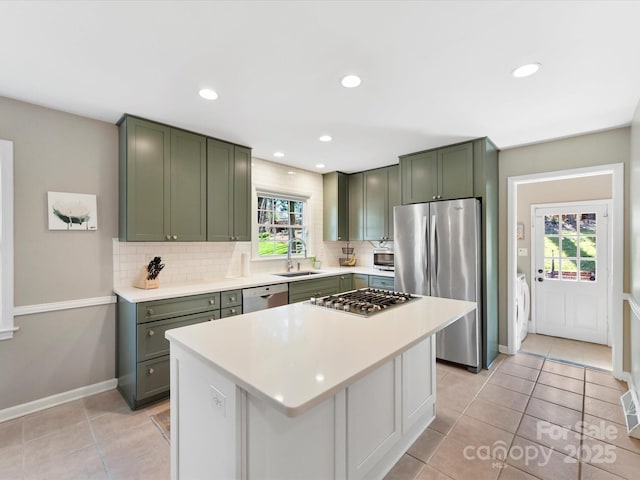 kitchen featuring washer and clothes dryer, a sink, stainless steel appliances, green cabinetry, and decorative backsplash