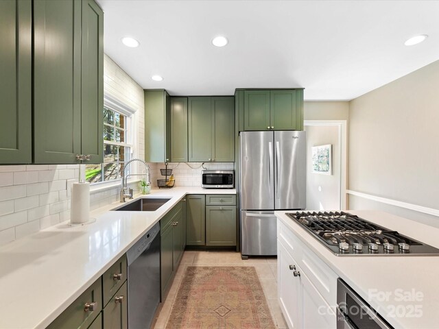 kitchen featuring a sink, light countertops, appliances with stainless steel finishes, green cabinets, and backsplash