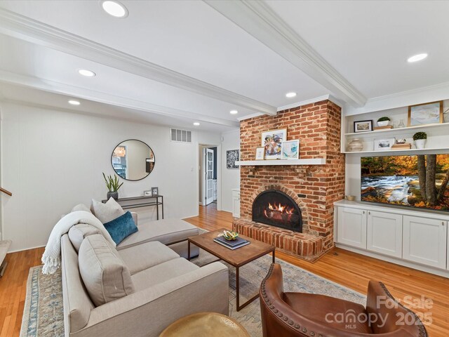 living area with crown molding, beamed ceiling, light wood-style flooring, and visible vents