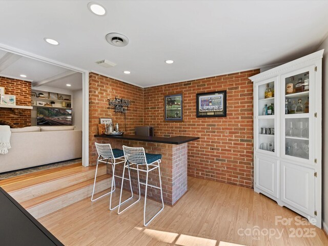 interior space with visible vents, light wood-style flooring, recessed lighting, a bar, and brick wall