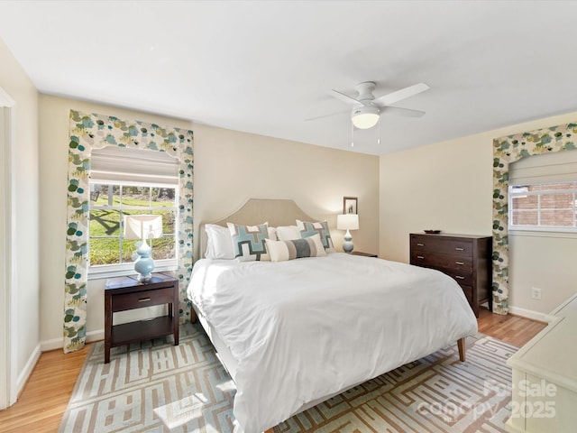 bedroom featuring light wood-type flooring, multiple windows, baseboards, and ceiling fan