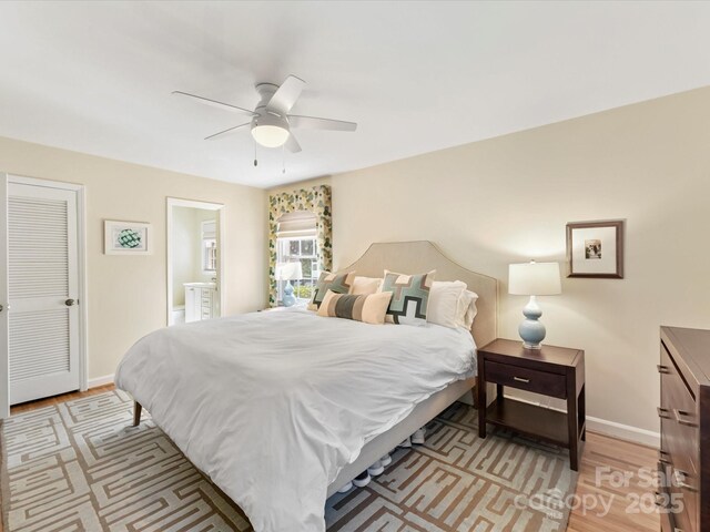 bedroom featuring light wood finished floors, ceiling fan, ensuite bath, and baseboards