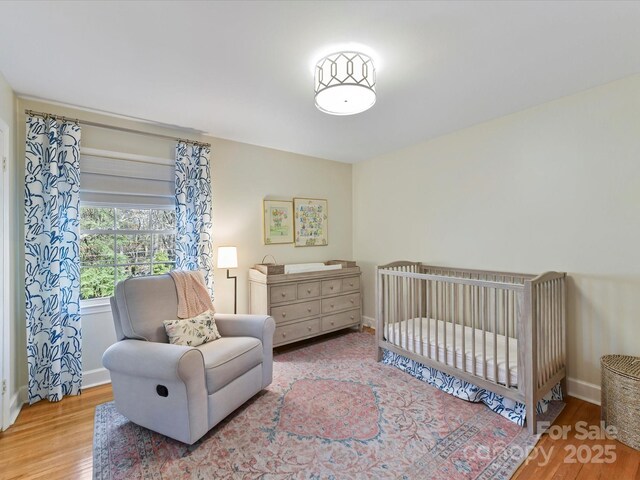 bedroom with a nursery area, wood finished floors, and baseboards