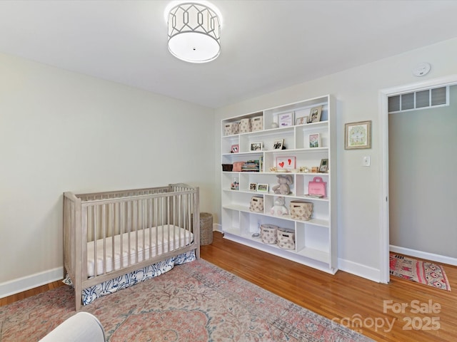 bedroom with a nursery area, wood finished floors, visible vents, and baseboards