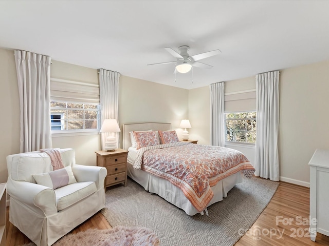 bedroom featuring multiple windows, a ceiling fan, baseboards, and wood finished floors