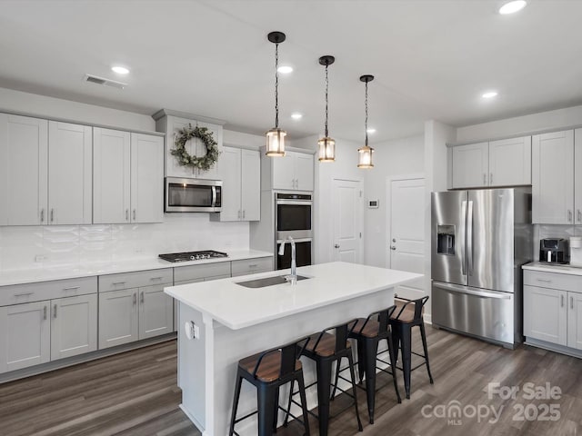 kitchen featuring stainless steel appliances, a breakfast bar, a sink, dark wood-style floors, and tasteful backsplash