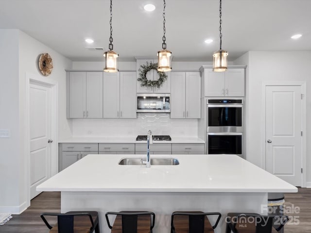 kitchen featuring dark wood-style floors, a breakfast bar, tasteful backsplash, appliances with stainless steel finishes, and a sink