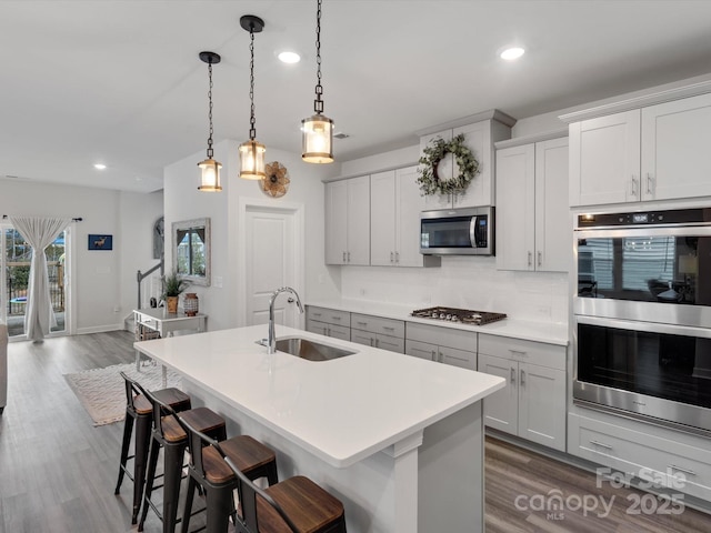 kitchen featuring a center island with sink, appliances with stainless steel finishes, a sink, light countertops, and backsplash