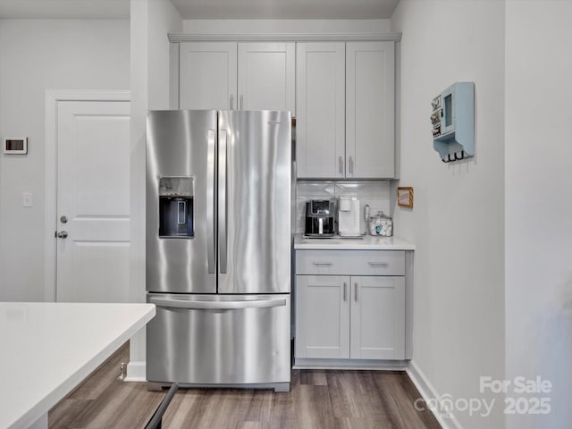 kitchen featuring baseboards, light countertops, stainless steel refrigerator with ice dispenser, dark wood-style floors, and tasteful backsplash