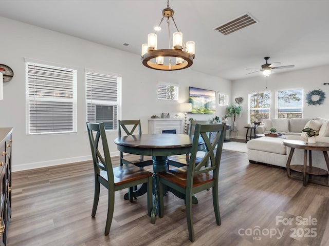 dining space with baseboards, visible vents, wood finished floors, and ceiling fan with notable chandelier