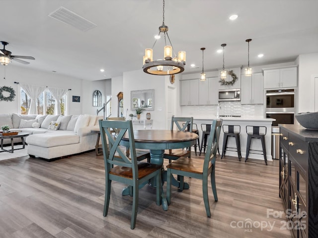 dining space with ceiling fan with notable chandelier, wood finished floors, visible vents, and recessed lighting