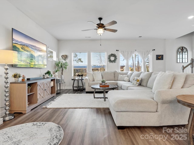 living room with a ceiling fan, a wealth of natural light, visible vents, and dark wood finished floors