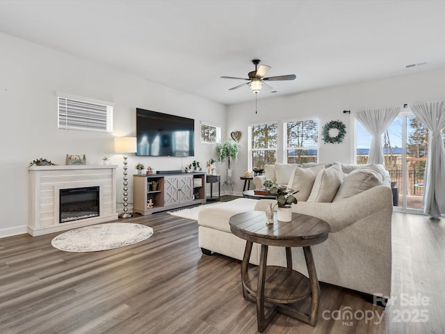 living room featuring baseboards, visible vents, a glass covered fireplace, ceiling fan, and wood finished floors