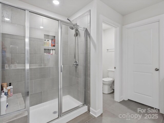 bathroom with toilet, a shower stall, and tile patterned flooring