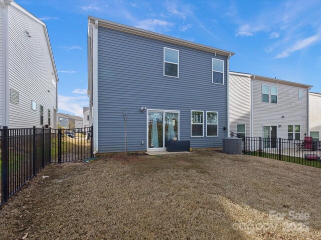 rear view of house featuring central air condition unit, a fenced backyard, and a lawn