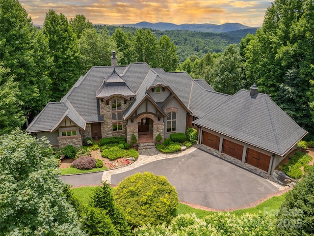 view of front of house with a mountain view, a garage, stone siding, driveway, and a chimney