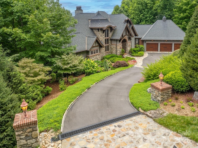 english style home featuring metal roof, a detached garage, stone siding, a standing seam roof, and a chimney