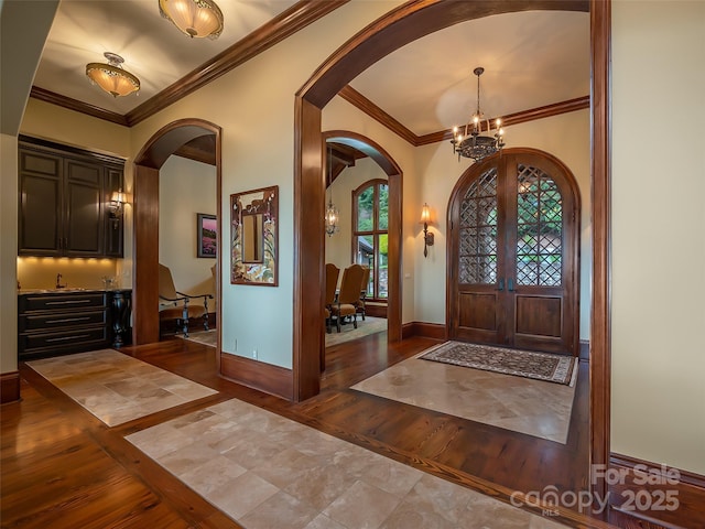 entryway featuring baseboards, arched walkways, ornamental molding, hardwood / wood-style floors, and a chandelier