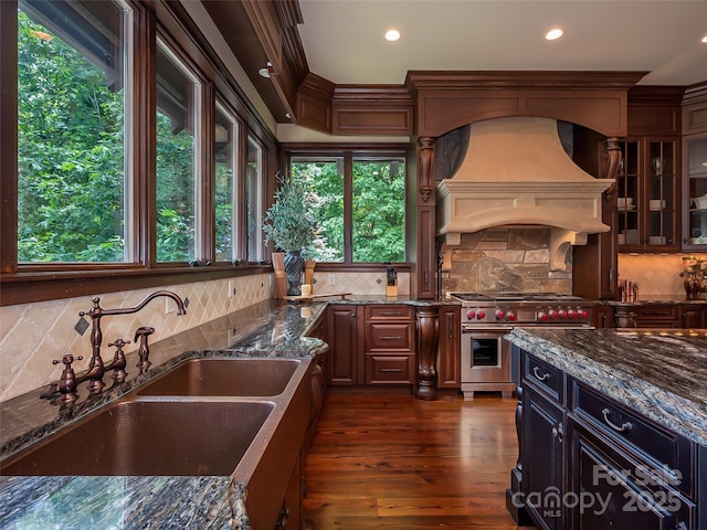 kitchen featuring range with two ovens, premium range hood, a sink, and decorative backsplash