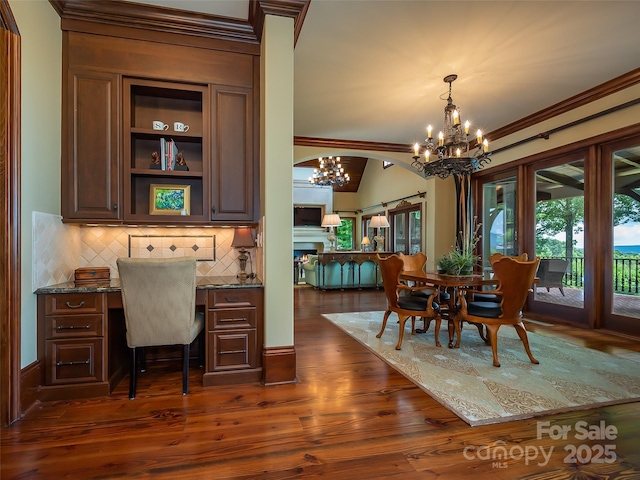 office with an inviting chandelier, dark wood-type flooring, ornamental molding, built in study area, and a warm lit fireplace