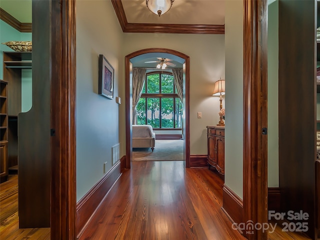 hall with baseboards, visible vents, arched walkways, ornamental molding, and wood finished floors