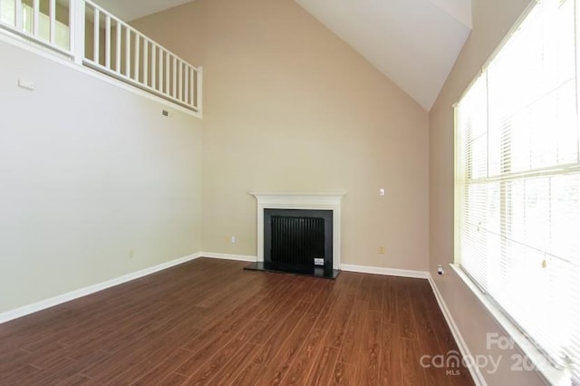 unfurnished living room featuring a fireplace with raised hearth, high vaulted ceiling, wood finished floors, and baseboards