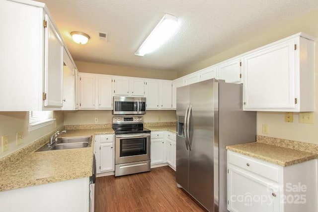 kitchen with dark wood finished floors, stainless steel appliances, light countertops, white cabinetry, and a sink